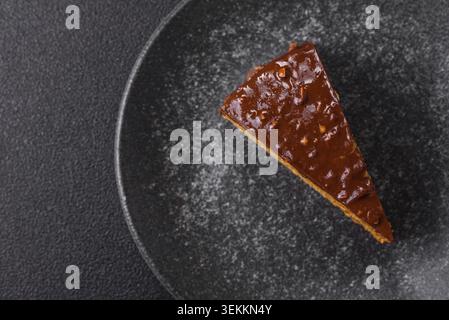 Una fetta di torta dolce a strati ricoperta di cioccolato con noci e caramello. Una fetta di torta al cioccolato come sfondo alimentare per il tuo design Foto Stock