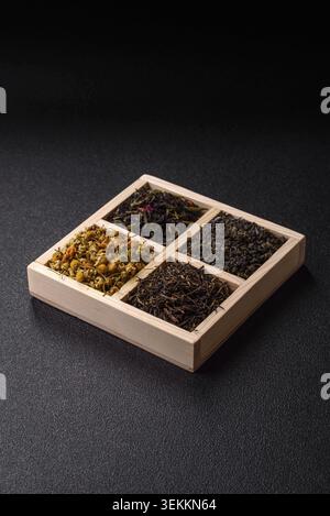 Una scatola di legno con diversi tipi di tè secco, verde, nero, frutta e camomilla. Asciugare il tè nella scatola come sfondo per il tuo design Foto Stock