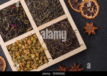 Una scatola di legno con diversi tipi di tè secco, verde, nero, frutta e camomilla. Asciugare il tè nella scatola come sfondo per il tuo design Foto Stock