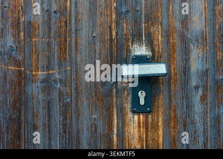 Primo piano di una moderna maniglia per porta in metallo scuro e di un foro per serratura montato su una parete rustica in legno con assi intemprati. Foto Stock
