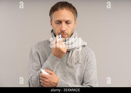 L'uomo malato con sistema immunitario indebolito controlla la temperatura con il termometro in bocca sente affaticamento da sintomi di malattia virale. Esausto malvagio maschio su Foto Stock