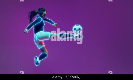 Determinata giocatrice di calcio femminile delineata con linee al neon che calciano la palla nello studio viola. Foto Stock