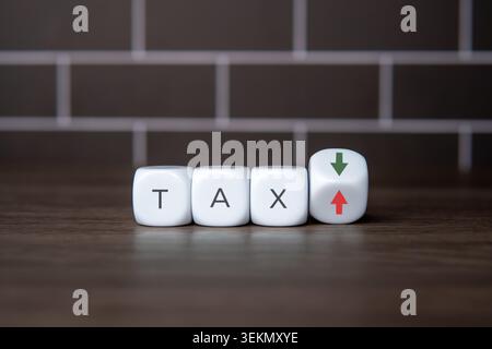 Blocchi bianchi che compongono la parola TAX accanto a un cubo inclinato con frecce verdi verso il basso e rosse verso l'alto. Sgravi fiscali, aumenti fiscali, pianificazione finanziaria, Foto Stock