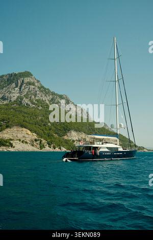 Yacht a vela di lusso ancorato vicino alla costa rocciosa del Mediterraneo in estate. Foto Stock