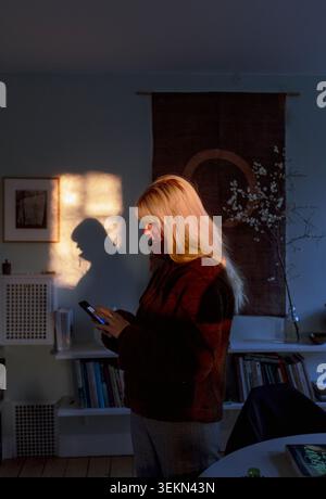 Donna bionda che usa lo smartphone mentre è a casa Foto Stock