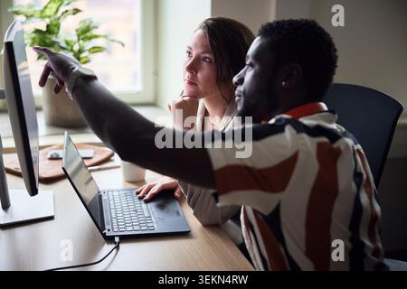 Visione ad angolo alto di una donna d'affari che ascolta un collega che spiega idee sul computer in ufficio Foto Stock