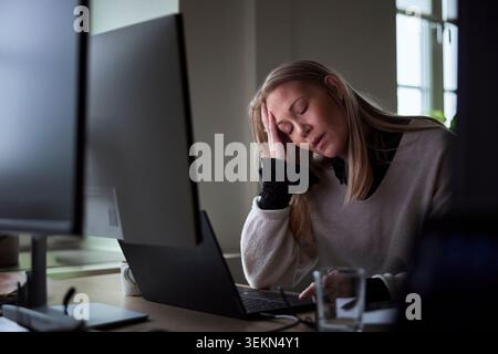 Imprenditrice stanca con gli occhi chiusi appoggiati al gomito nell'ufficio tecnico Foto Stock