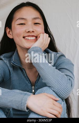 Ritratto di una giovane donna sorridente seduta mentre si appoggia al gomito Foto Stock
