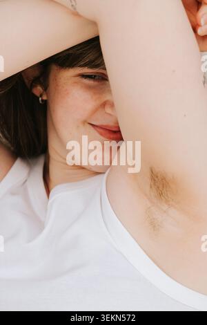 Giovane donna sorridente e sicura di sé che mostra i capelli delle ascelle Foto Stock