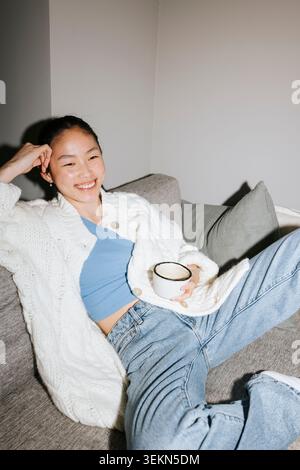 Vista dall'alto della giovane donna sorridente seduta sul divano di casa Foto Stock