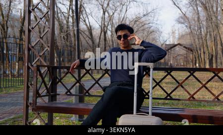 Giovane uomo rilassato e sicuro di sé seduto su una panchina di legno Foto Stock