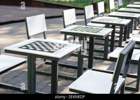 Tavoli da scacchi vuoti con sedie in un parco pubblico cittadino in una giornata di sole. File di campi da scacchi vuoti sui tavoli in un parco urbano estivo. Foto Stock