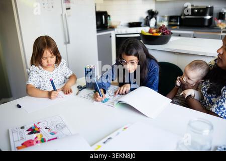 Vista ad angolo alto delle bambine che colorano mentre seduto con la madre e il fratello del bambino al tavolo di casa Foto Stock