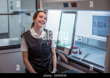 Giovane scienziato sorridente seduto vicino a un armadietto laminare in laboratorio Foto Stock