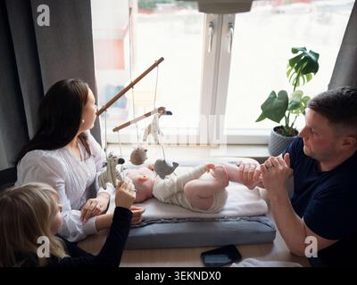 Vista ad angolo alto della ragazza che gioca con il fratellino mentre i genitori sono seduti al tavolo a casa Foto Stock