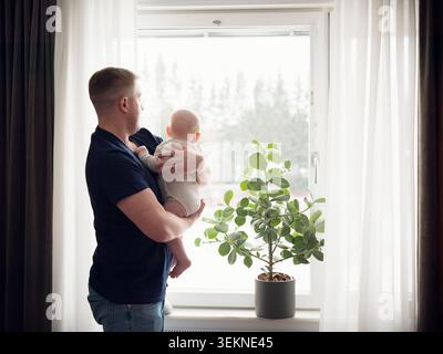 Padre e figlio che guardano fuori dalla finestra di casa Foto Stock