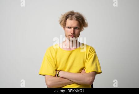 Giovane che mostra un'espressione diffidente e sospetta, solleva le sopracciglia, si sente scettico, dubita, interroga, e avere le braccia incrociate in studio Foto Stock