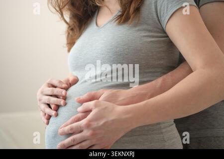 Donna incinta e marito che tengono insieme la pancia in un intimo primo piano. Aspettarsi la madre con il partner che culla lo stomaco come simbolo di responsabilità condivisa. La futura mamma crea un legame con il nascituro Foto Stock