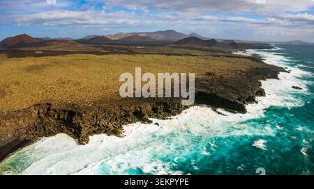 La vista aerea cattura la costa di El Golfo a Lanzarote con il suo terreno vulcanico e le onde che si infrangono contro le formazioni rocciose. La scena Foto Stock