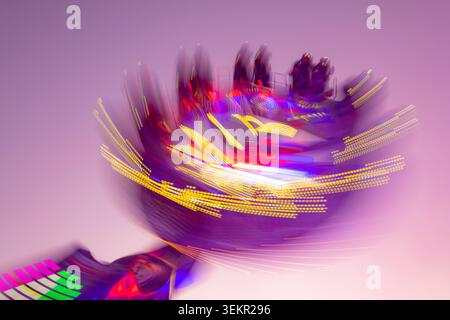Carosello in pieno svolgimento: Foto a lunga esposizione in una fiera tedesca al crepuscolo. Colorate tracce di luce dal giro in rotazione durante la rotazione. Funfa in movimento Foto Stock