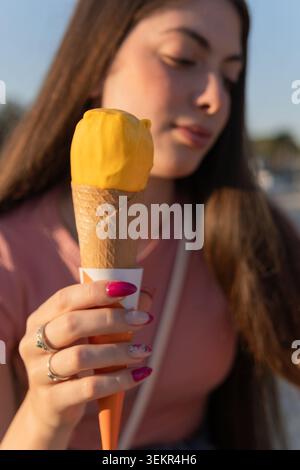 Una donna che tiene un cono di gelato. Indossa una camicia rosa e ha i capelli lunghi Foto Stock