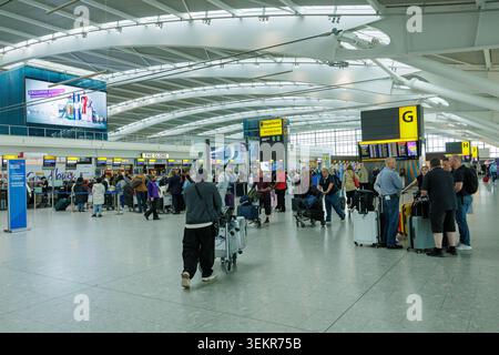 I passeggeri in piedi con bagagli pesanti e valigie in coda al check-in all'interno del terminal dell'aeroporto di Londra Heathrow, Regno Unito. Foto Stock