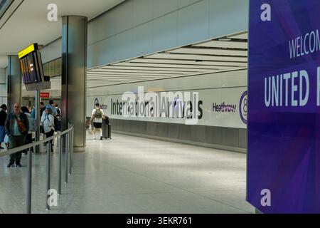 Vista prospettica dei passeggeri che passano davanti al cartello con la scritta International Arrivals all'interno del terminal dell'aeroporto di Londra Heathrow, Regno Unito. Foto Stock