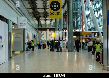 Passanti e personale di terra che cammina attraverso l'atrio degli arrivi sud con un negozio di caffè Nero presso l'aeroporto Heathrow di Londra, Regno Unito. Foto Stock