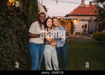 Diverse amiche femminili che si godono una festa in giardino con bevande Foto Stock