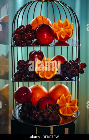 Servizio in camera di lusso, vassoio di frutta di benvenuto con agrumi freschi, mele e uva rossa elegantemente disposti su un piatto creativo Foto Stock