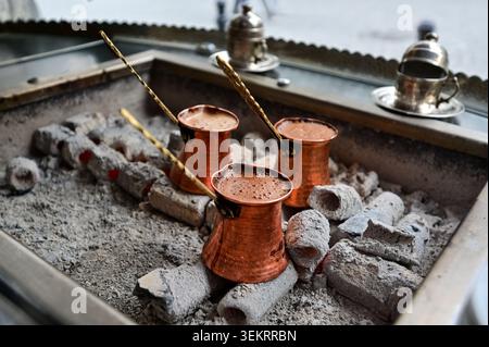 Caffè turco tradizionale in pentole di rame che si preparano su carboni brillanti, primo piano con manici in schiuma e ottone, autentico caffè di strada in Turchia. Foto Stock