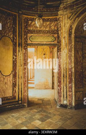 AGLIÈ, ITALIA – OTTOBRE 2025: Vista interna del castello di Agliè con pareti dipinte ornate, marmi invecchiati e porte che conducono a un corrido illuminato dal sole Foto Stock