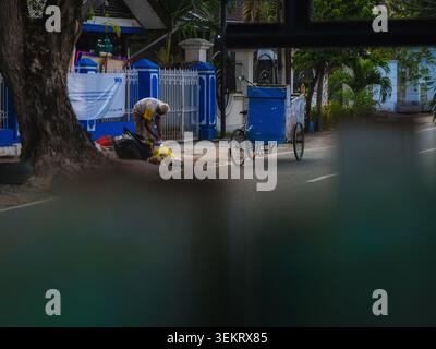 Palu, Indonesia - 31 maggio 2026: Candid ha sparato a un vecchio che raccoglieva e smistava bottiglie di plastica dai sacchetti della spazzatura nel suo carrello triciclo in una strada suburbana in Indonesia. Immagine concettuale della povertà, del duro lavoro e del riciclaggio ambientale con un primo piano sfocato. Foto Stock
