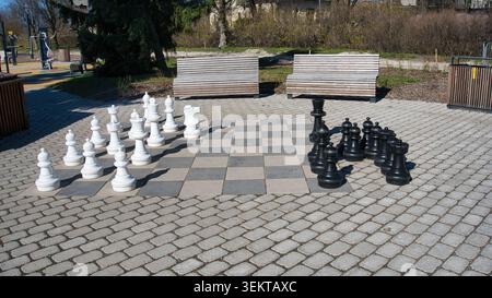Gigantesco scacchi all'aperto in un parco pubblico cittadino con panchine di legno Foto Stock
