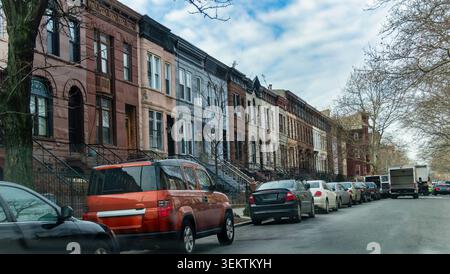 New York, Stati Uniti, 15 gennaio 2015, una linea di storiche case a più piani in pietra arenaria e mattoni si erge lungo una strada residenziale della città con diverse auto Foto Stock