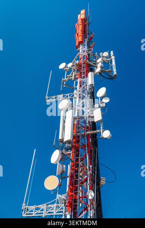 Torre di comunicazione cellulare con più antenne e trasmettitori contro il cielo azzurro Foto Stock