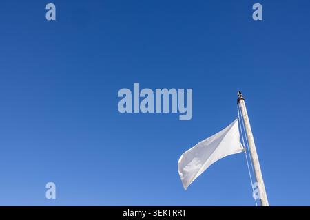 Bandiera bianca bianca che sventola su un palo di legno contro un cielo azzurro con ampio spazio per le copie adatto per il branding, la pubblicità, i concept di design e le comunicazioni Foto Stock