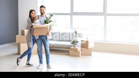 Una giovane coppia che tiene in mano una scatola mobile con piante d'appartamento e orologio in un luminoso nuovo appartamento, sorridendo proprietari di case in piedi tra scatole di cartone nella vita moderna Foto Stock