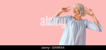 Donna anziana felice con i capelli grigi che fanno segni di pace e ridendo, allegro ritratto femminile maturo isolato su sfondo rosa con spazio fotocopie, positi Foto Stock