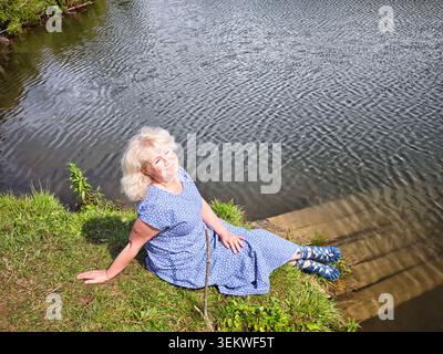 Donna bionda matura che si gode un momento tranquillo sul fiume durante la sua avventura di viaggio Foto Stock