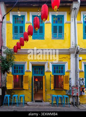 Kuala Lumpur, Malesia - 21 febbraio 2025: Vivace negozio giallo con finestre blu, lanterne cinesi rosse e sgabelli blu a Chinatown Foto Stock