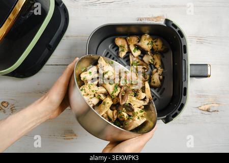 Versare funghi di ostriche marinati nel recipiente della friggitrice ad aria. Preparazione di piatto sano. Le erbe fresche vengono mescolate per conferire un sapore ancora maggiore. Foto Stock