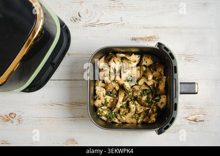 I funghi di ostrica freschi vengono tritati e collocati nel cestello della friggitrice ad aria. La friggitrice ad aria compressa è posizionata su un piano cucina, pronta per cucinare piatti semplici e sani Foto Stock