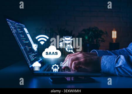 Concetto SaaS con notebook, icone cloud e attività pratiche di lavoro sul software di notte Foto Stock