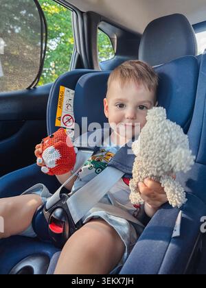 Il bambino è fissato in un seggiolino per auto con peluche Foto Stock