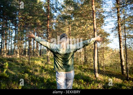 Donna attiva amante della natura che cammina nei boschi, si erge a braccia aperte nella foresta godendosi il paesaggio Foto Stock