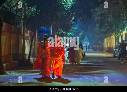 Due donne indiane che camminano lungo una strada notturna. Foto Stock