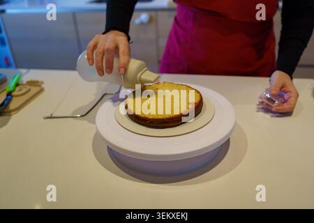 Lo chef inzuppa uno strato di pan di Spagna con sciroppo semplice su un tavolo girevole per torte Foto Stock