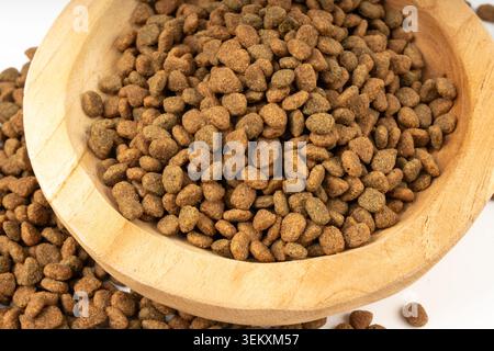 Primo piano di cibo secco per animali domestici, pila di kibble per cani in una ciotola di legno, macchie di cucciolo, piccola farina di croquette di proteine canine, granuli di cibo per animali su dorso sfocato Foto Stock