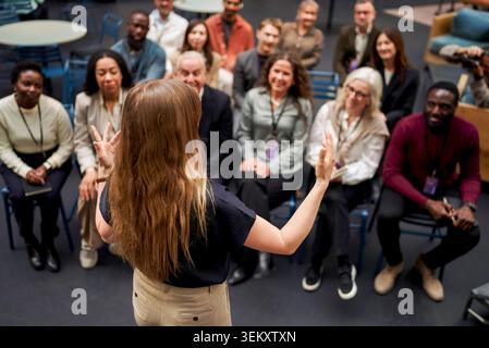 Vista posteriore ad angolo elevato dell'altoparlante femminile dai capelli lunghi che gestisce con le mani mentre comunica con il pubblico durante le convention Foto Stock
